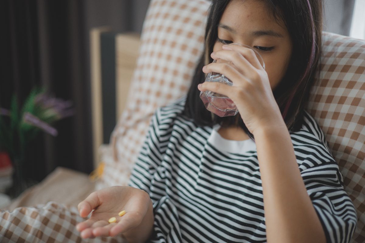 A girl taking vitamins recommended for kids while drinking water
